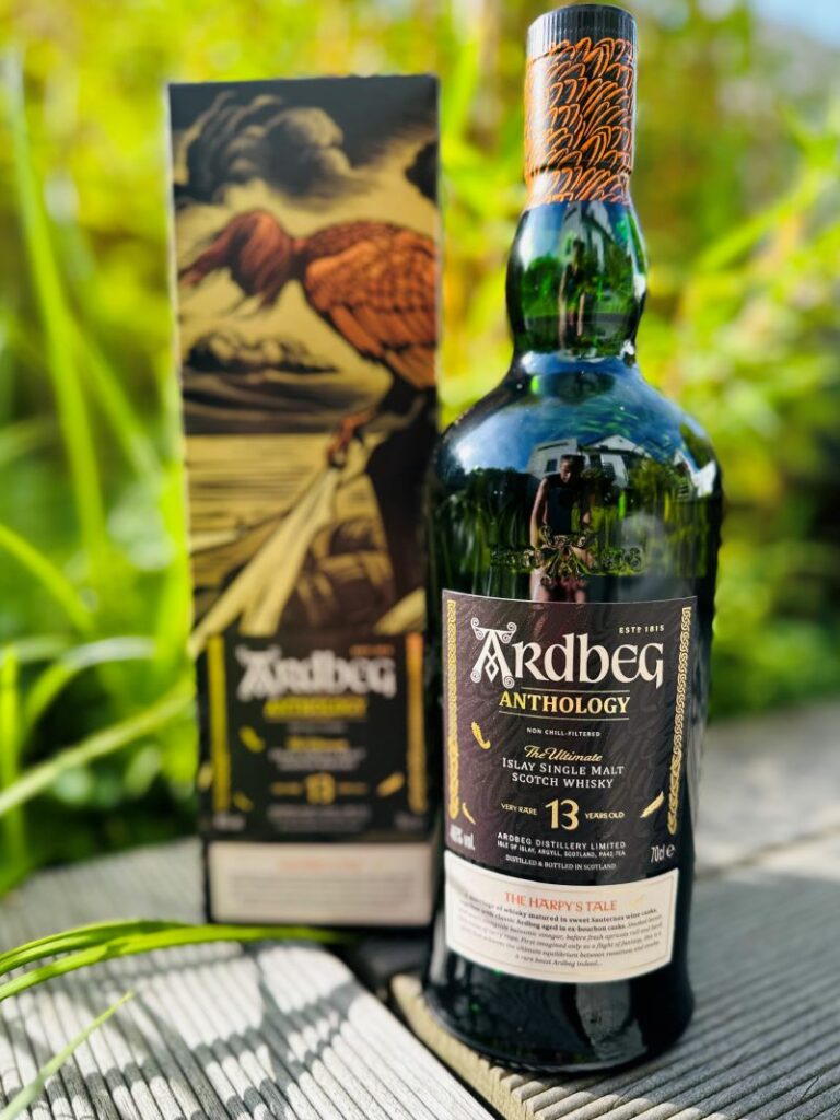 Eine Flasche Ardbeg Anthology 13 Years Single Malt Scotch Whisky mit Geschenkverpackung steht vor Gräsern.